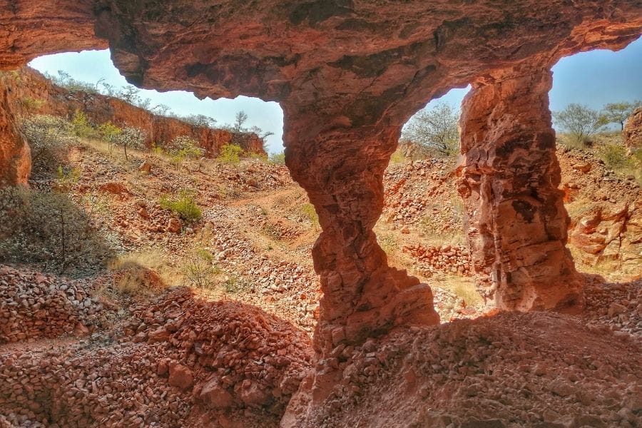 Spectacular red rock formations create natural arches, framing a rugged landscape with sparse vegetation under a clear blue sky. No people or buildings visible.